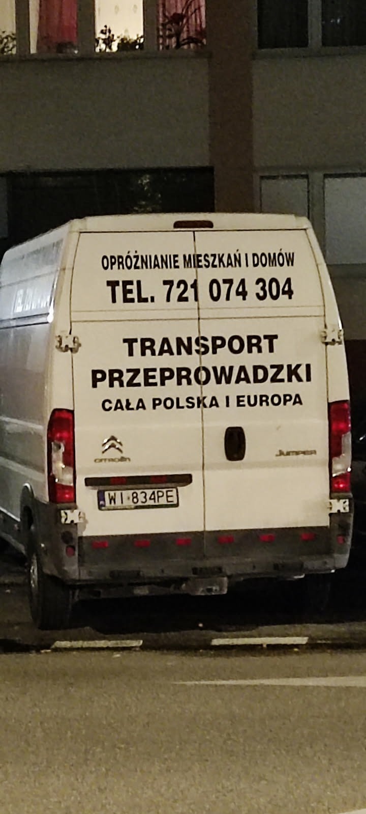 Biały bus Citroen Jumper z numerem telefonu i napisem 'Transport Przeprowadzki' oraz 'Opróżnianie mieszkań i domów' na tle budynku.