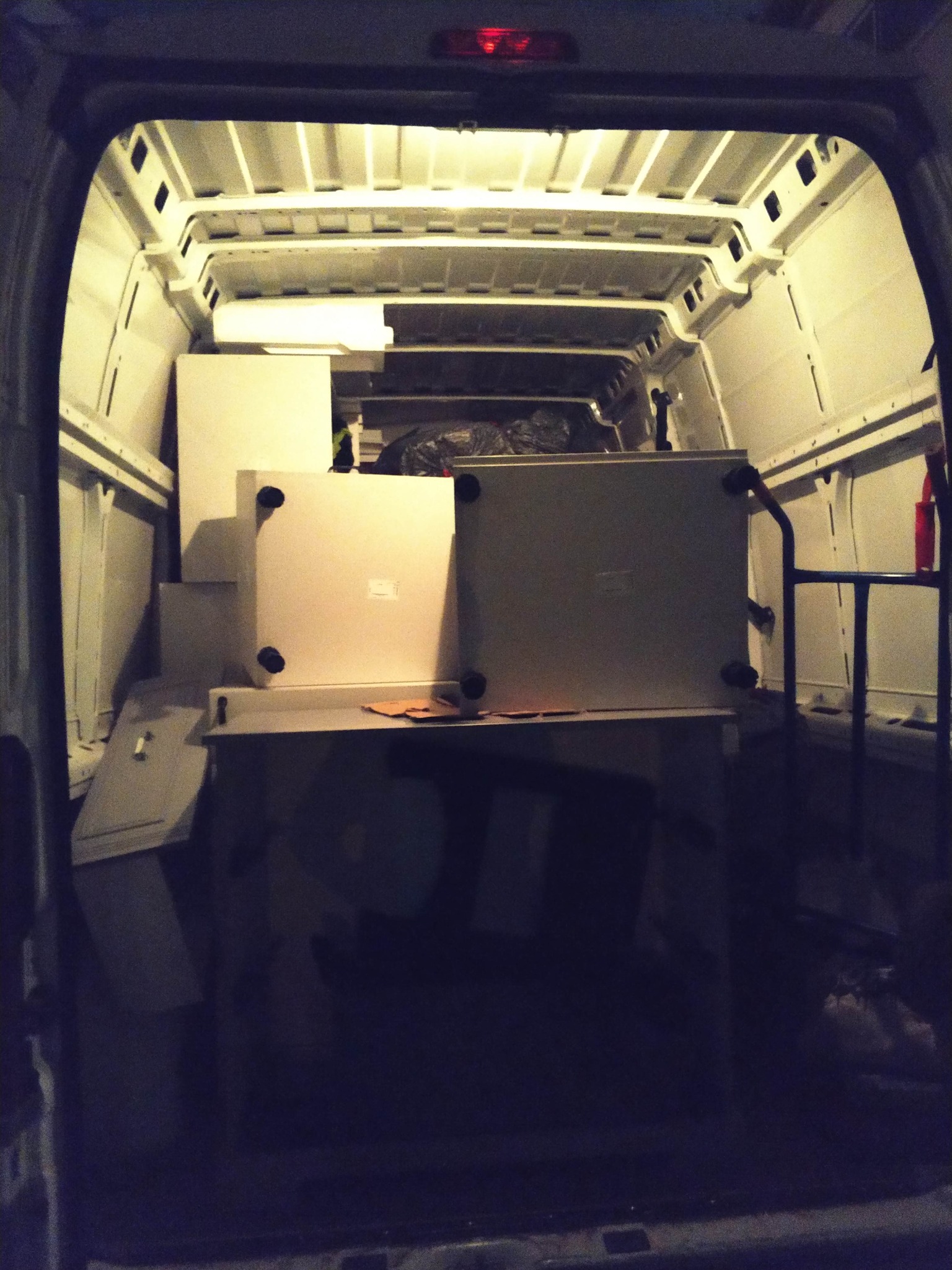 Wnętrze busa wypełnione meblami podczas transportu. Widoczne białe szafki i inne elementy wyposażenia zabezpieczone w przestrzeni ładunkowej.