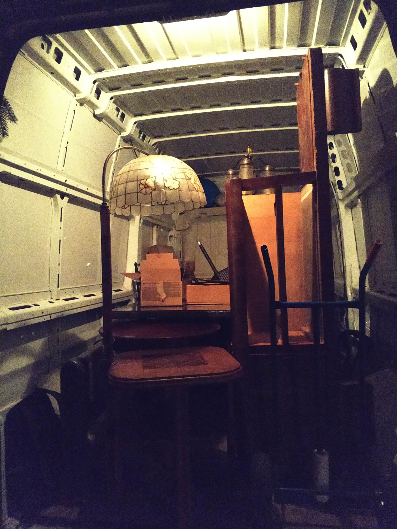 Wnętrze busa załadowane meblami i lampą Tiffany, gotowe do transportu. Widoczne kartony i wózek transportowy.
