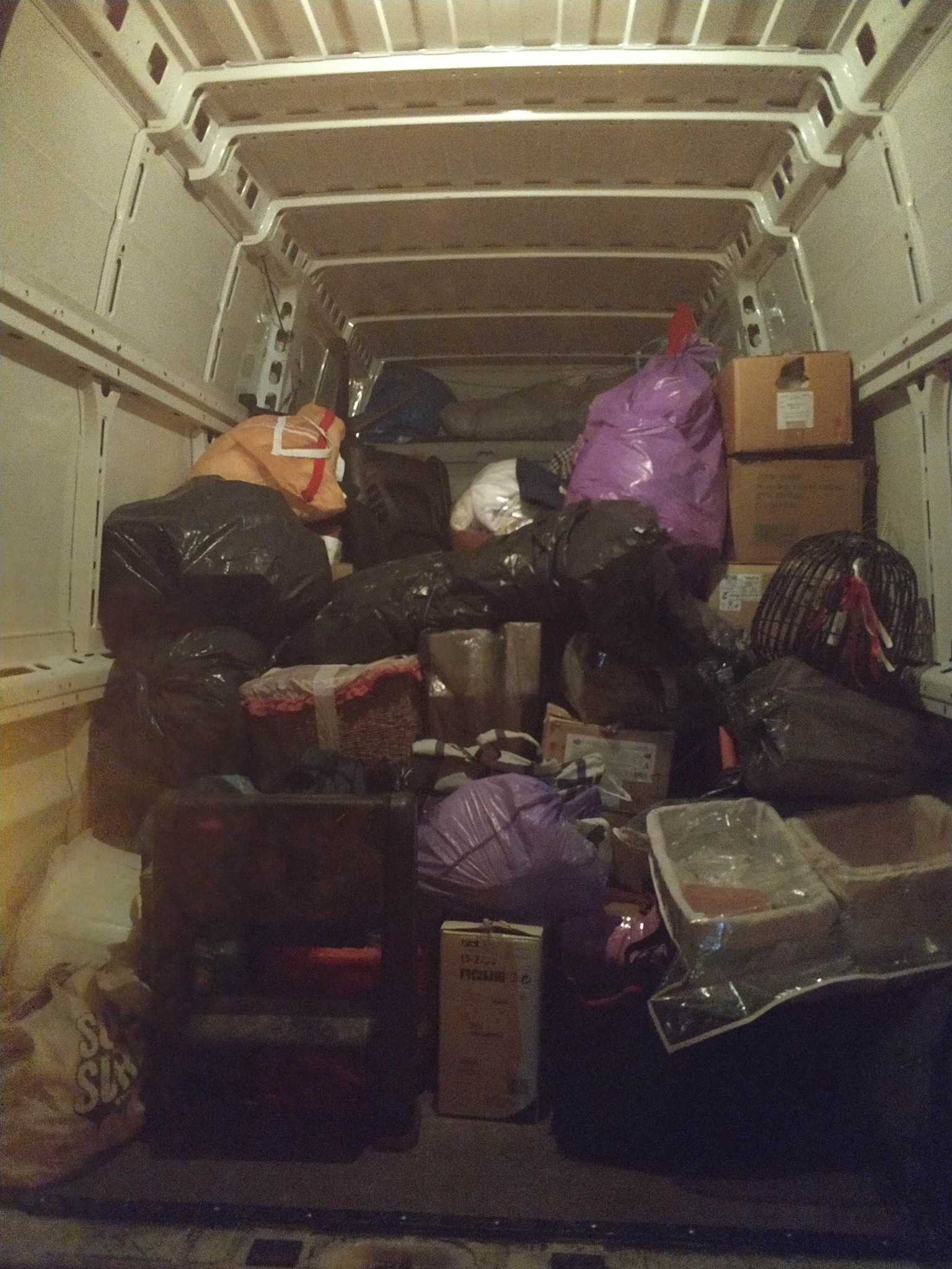 Wnętrze busa wypełnione po brzegi workami i kartonami, gotowe do transportu. Widok z tyłu pojazdu, ciemne oświetlenie.