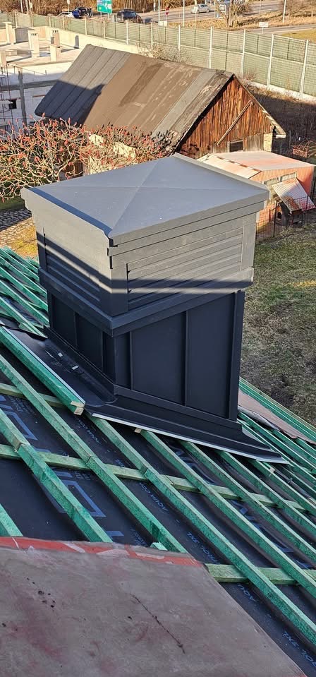 Nowoczesny komin wentylacyjny na dachu z łatami w Białymstoku. Czarny, kwadratowy komin z daszkiem, widok z góry na konstrukcję dachu przed pokryciem.