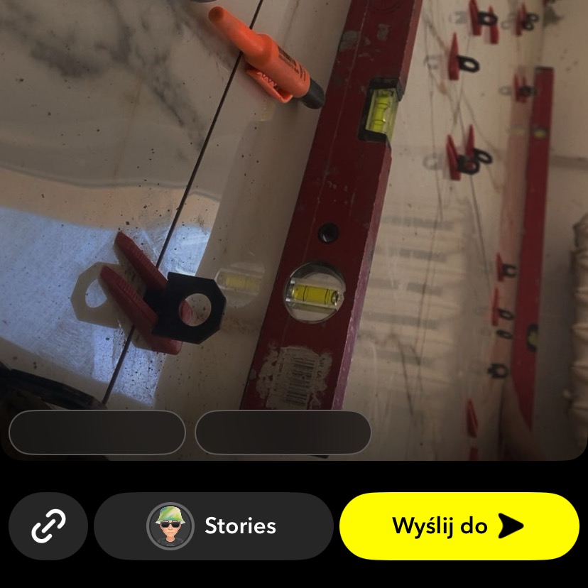 Poziomica, marker i klipsy do płytek na błyszczącej powierzchni. Układanie płytek z użyciem narzędzi i systemu poziomowania płytek.