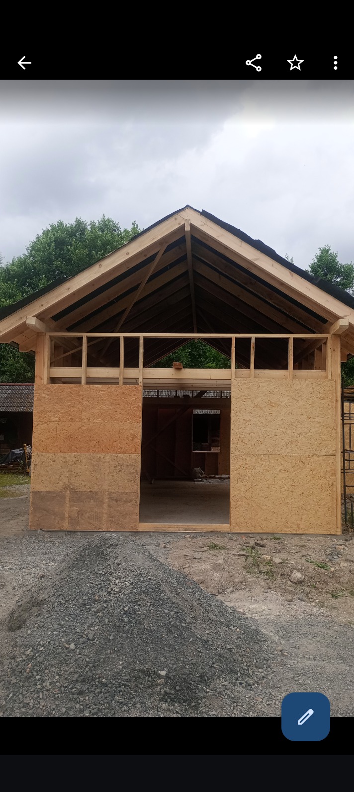 Konstrukcja szkieletowa budynku z widocznym dachem w trakcie budowy, z fragmentami płyt OSB na ścianach i stertą gruzu przed budynkiem.