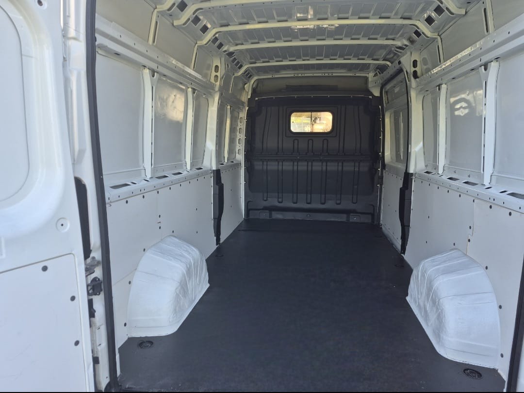 Wnętrze białego, pustego busa z czarną podłogą, przygotowanego do transportu. Widok z otwartych tylnych drzwi, ukazujący przestrzeń ładunkową i zabezpieczenia ścian.