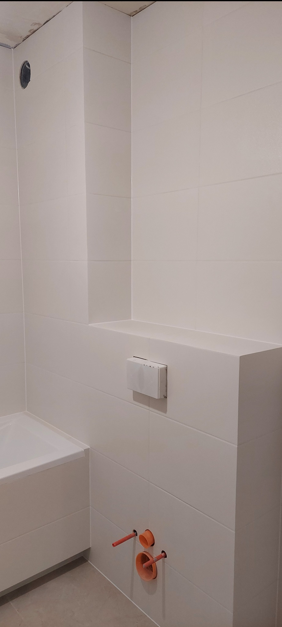 Biała łazienka po remoncie: widok na wannę, zabudowę geberitu i wyprowadzone instalacje wod-kan. Minimalistyczny design, jasne płytki, czyste linie.