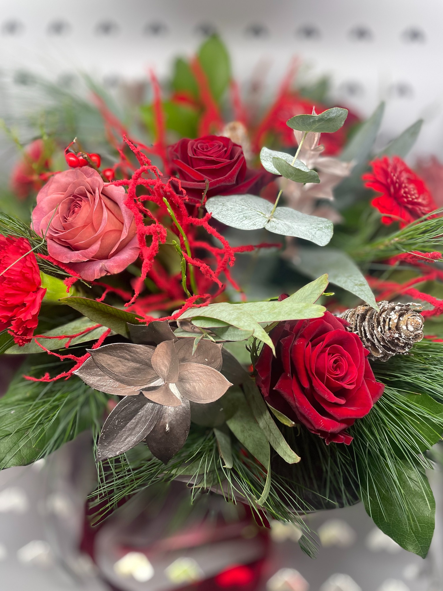 Dekoracyjny bukiet z czerwonych róż, świerkowych gałązek i srebrzonych szyszek, wykonany w Bydgoszczy. Idealny na prezent lub świąteczną ozdobę.
