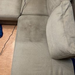 OgarnieMyto - Częściowo wyczyszczona, beżowa kanapa z widocznym efektem prania tapicerki na siedzisku. Na podłodze widoczny fragment kabla i niebieskiej tkaniny.