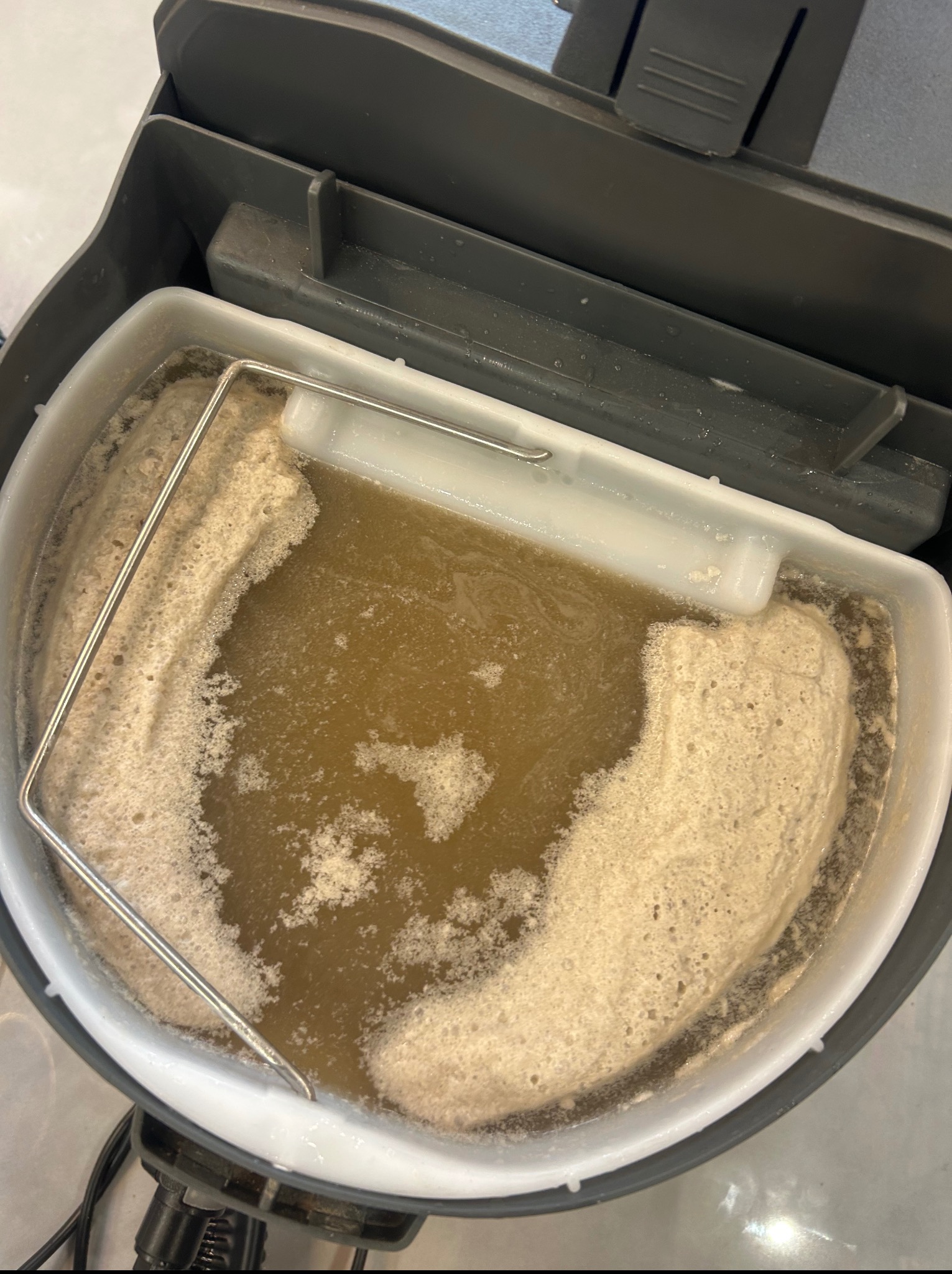 Brudna woda po praniu tapicerki w pojemniku odkurzacza. Widoczna piana i zanieczyszczenia. Ujęcie z góry na zawartość pojemnika po czyszczeniu.