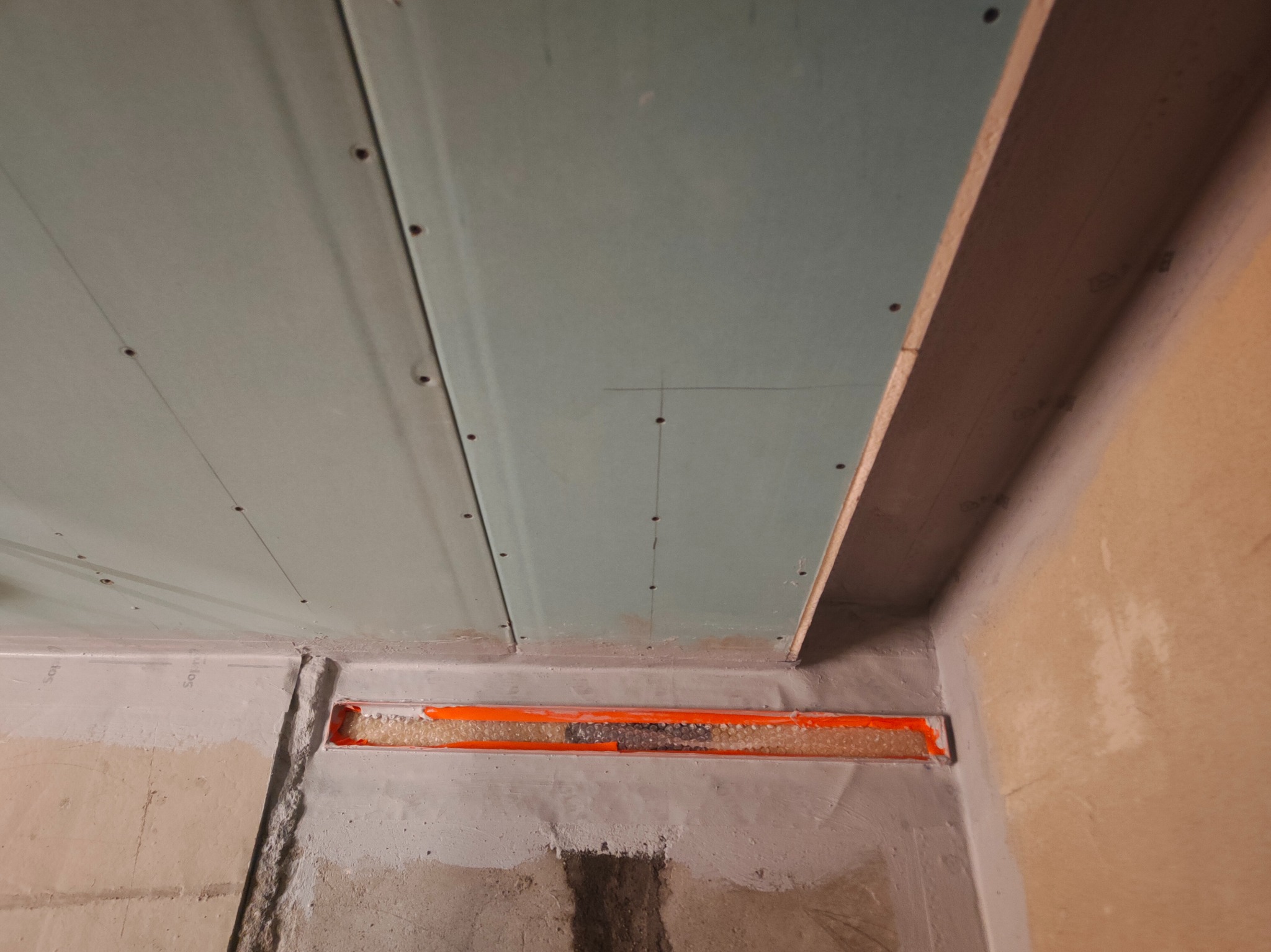 Montaż płyt gipsowo-kartonowych na suficie z widoczną izolacją w szczelinie. Detal wykończenia wnętrza w trakcie prac budowlanych.