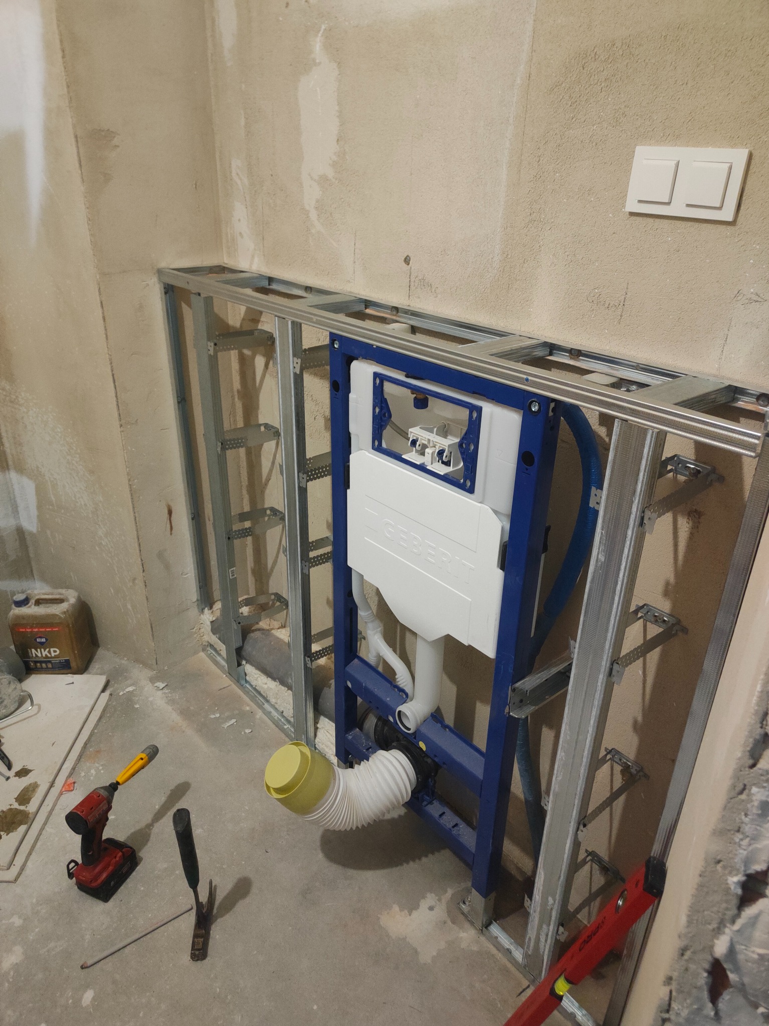 Montaż stelaża podtynkowego Geberit w łazience. Widoczne narzędzia, rury i elementy konstrukcyjne. Ściany w stanie surowym, instalacja w trakcie realizacji.