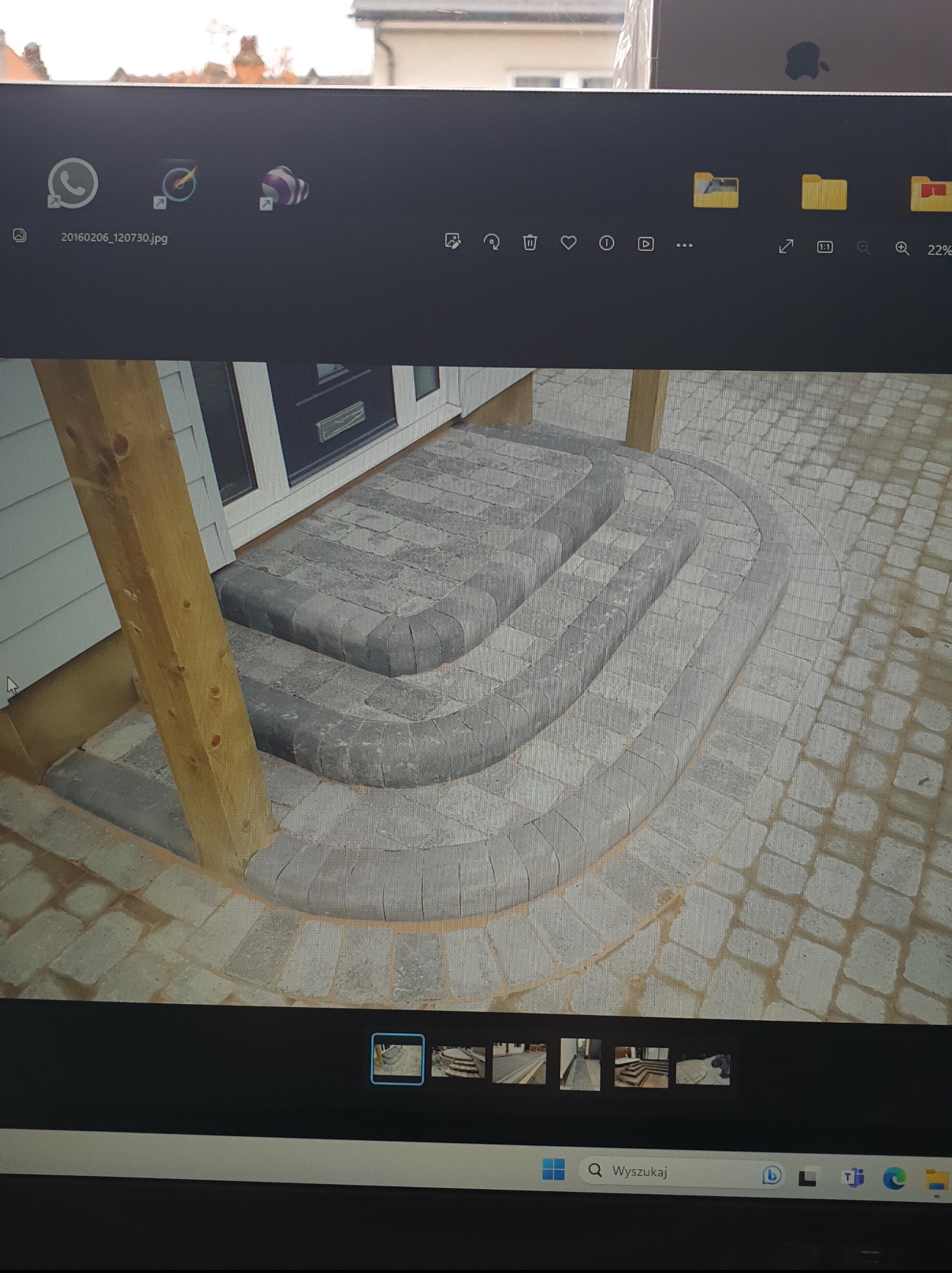 Schody wejściowe z kostki brukowej w odcieniach szarości, z zaokrąglonymi krawędziami i drewnianym słupem, prowadzące do drzwi wejściowych.