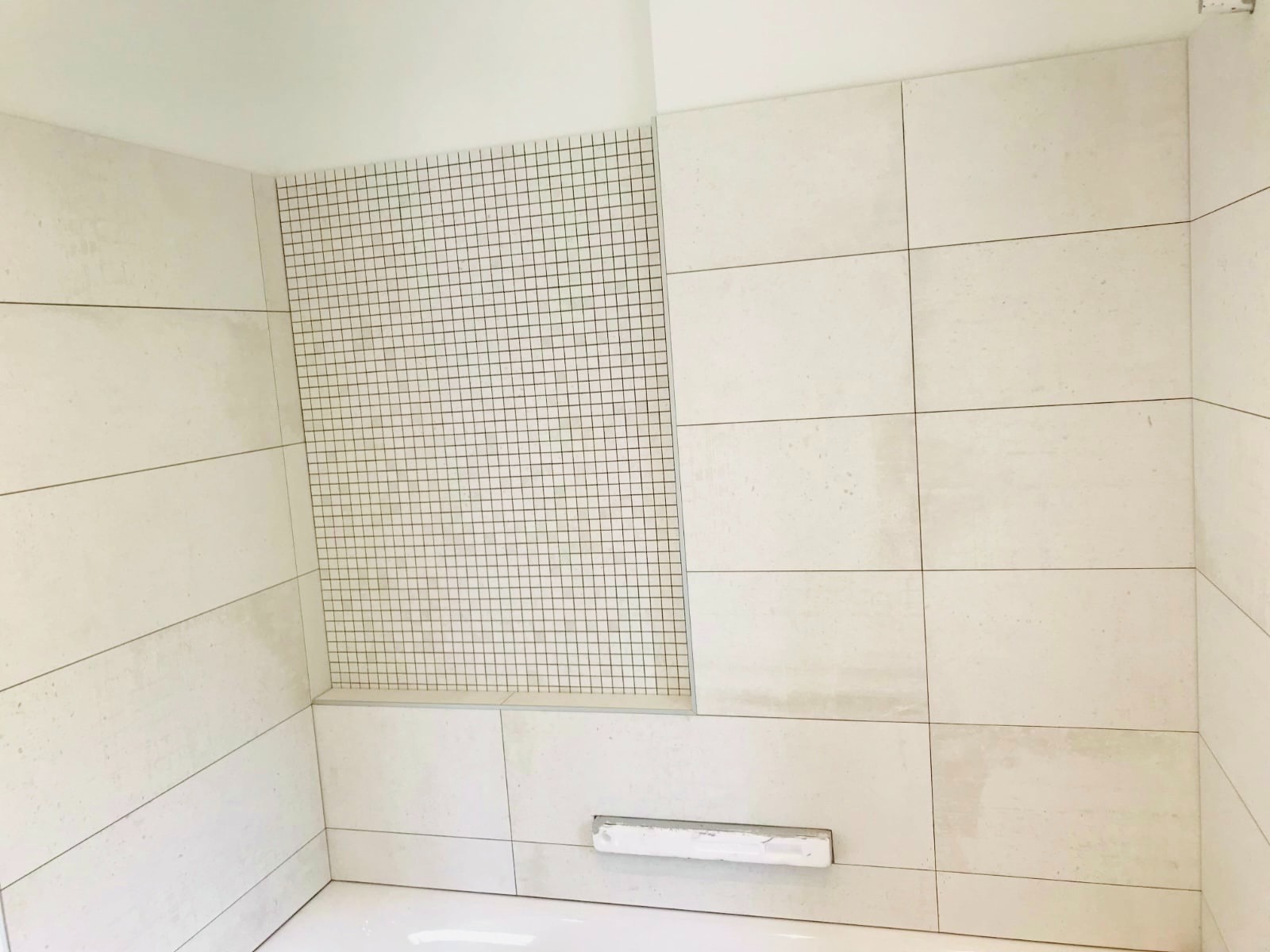 Jasna łazienka z mozaiką i dużymi, beżowymi płytkami ułożonymi poziomo. Widok na narożnik nad wanną.