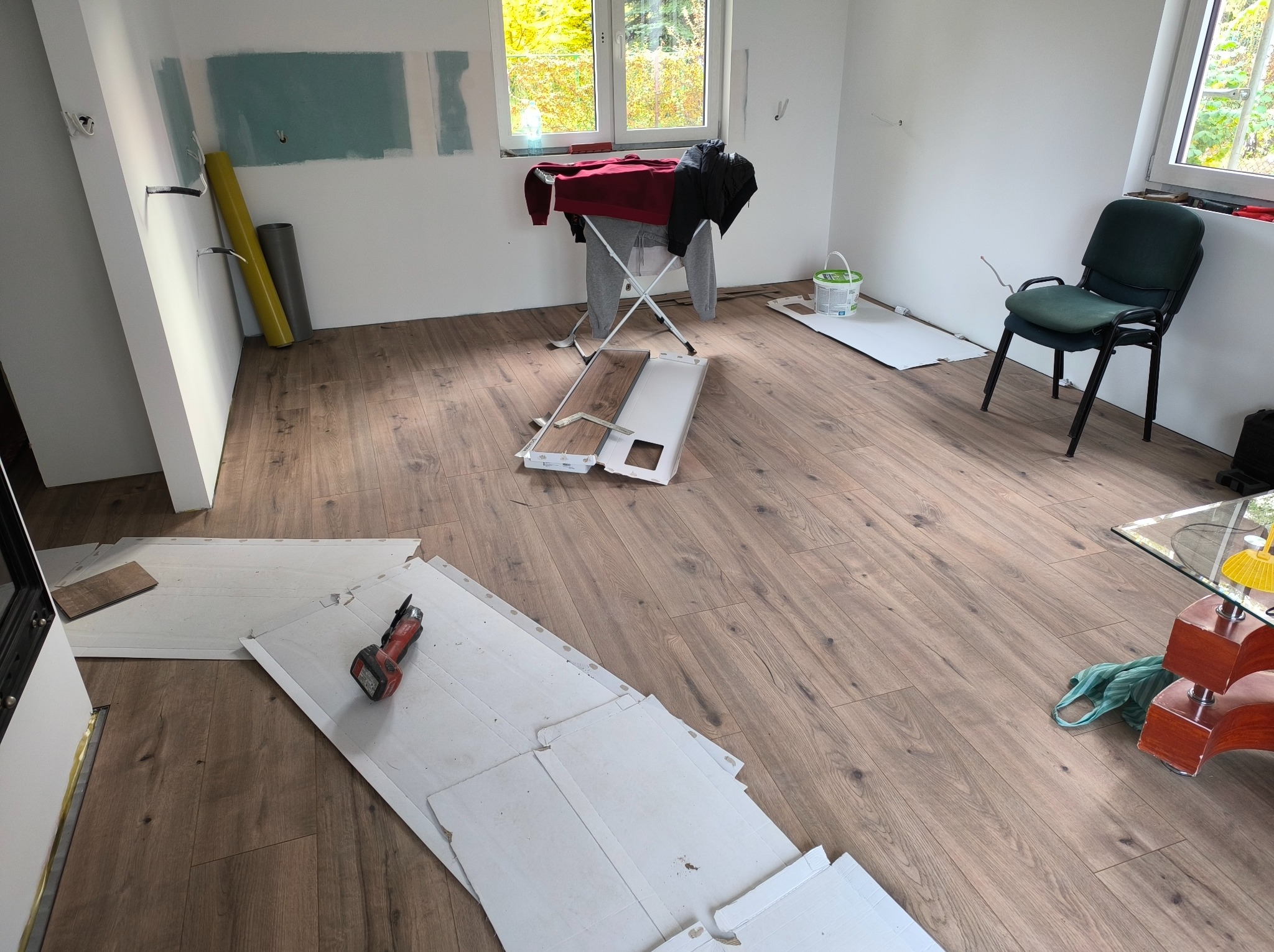 Pokój w trakcie układania paneli podłogowych. Widoczne panele, narzędzia oraz fragmenty ścian z widocznymi śladami po pracach wykończeniowych.