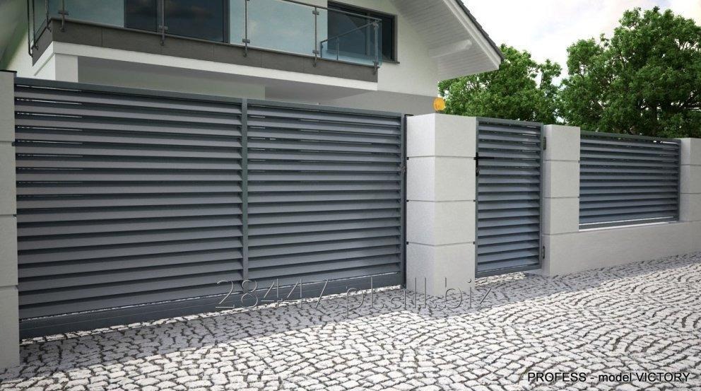 Nowoczesne, szare ogrodzenie lamelowe z betonowymi słupkami na tle domu z balkonem. Kostka brukowa na podjeździe. Model Victory.