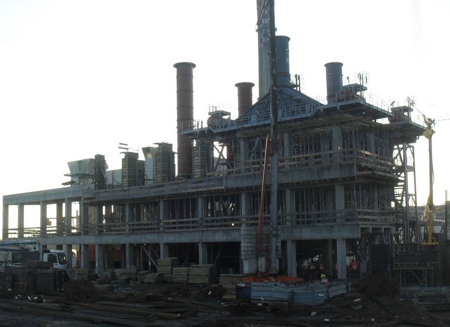 Konstrukcja żelbetowa w trakcie budowy, widoczne szalunki, zbrojenia i elementy konstrukcyjne. Na pierwszym planie składowane materiały budowlane.