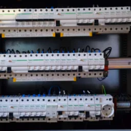 Rozdzielnica elektryczna z zainstalowanymi bezpiecznikami Schneider, widoczne przewody i gniazdo. Elementy zamontowane w metalowej obudowie.