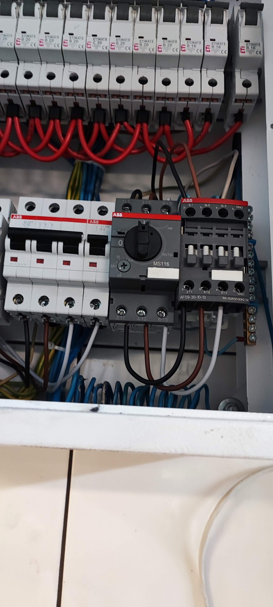 Rozdzielnia elektryczna z zainstalowanymi bezpiecznikami ETI i elementami ABB, widoczne kable w kolorach czerwonym, niebieskim, żółtym i brązowym.