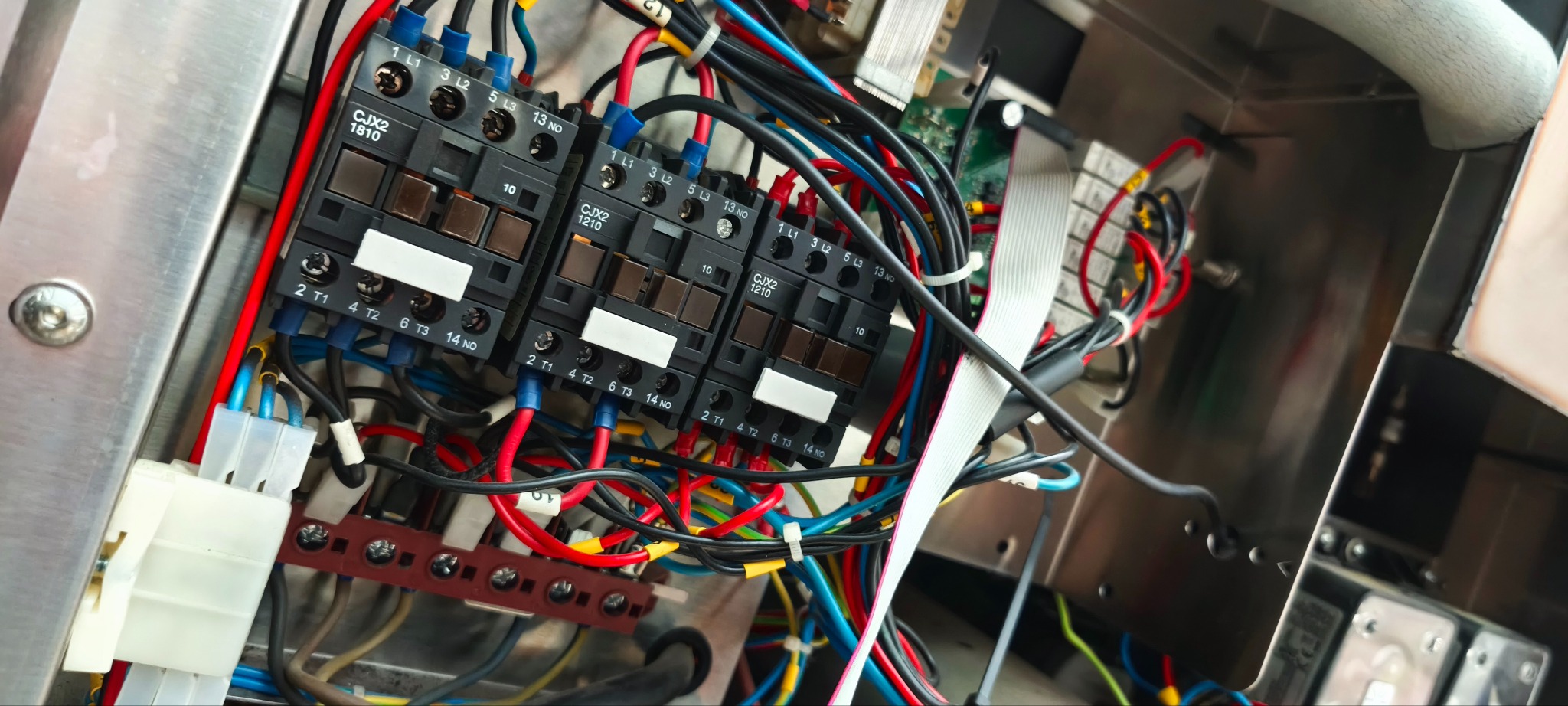 Panel elektryczny z trzema stycznikami CJX2 1210 i 1810, okablowaniem w kolorach: czerwonym, niebieskim, żółtym i czarnym, zamontowany na metalowej powierzchni.