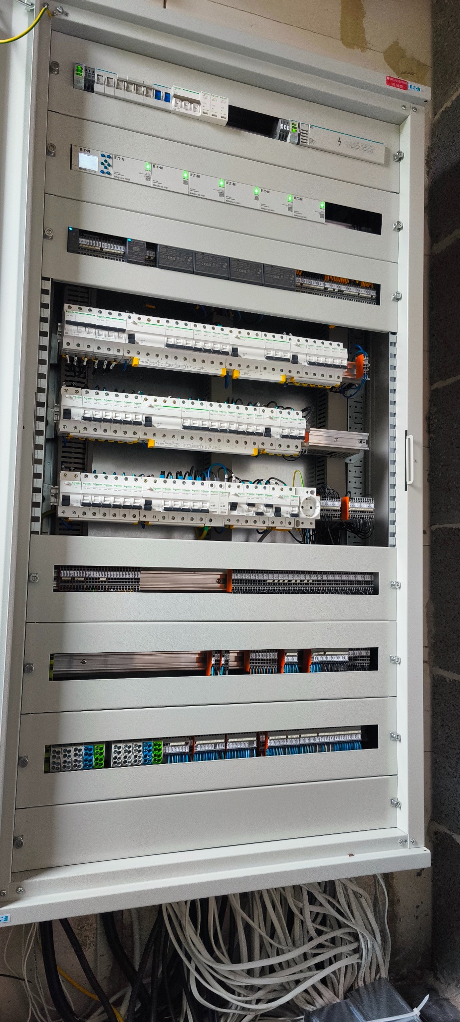 Rozdzielnica elektryczna z zainstalowanymi bezpiecznikami, modułami i przewodami. Widoczne elementy marki Eaton i Schneider. Przewody ułożone w dolnej części szafy.