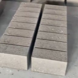 BAU-CONSTRUCTING SPÓŁKA Z OGRANICZONĄ ODPOWIEDZIALNOŚCIĄ - Dwa stosy szarych bloczków betonowych ułożone równolegle na szarej, betonowej powierzchni. Widoczne poziome żłobienia na bloczkach.