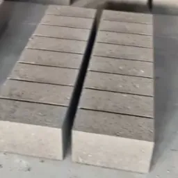 Dwa stosy szarych bloczków betonowych ułożone równolegle na szarej, betonowej powierzchni. Widoczne poziome żłobienia na bloczkach.