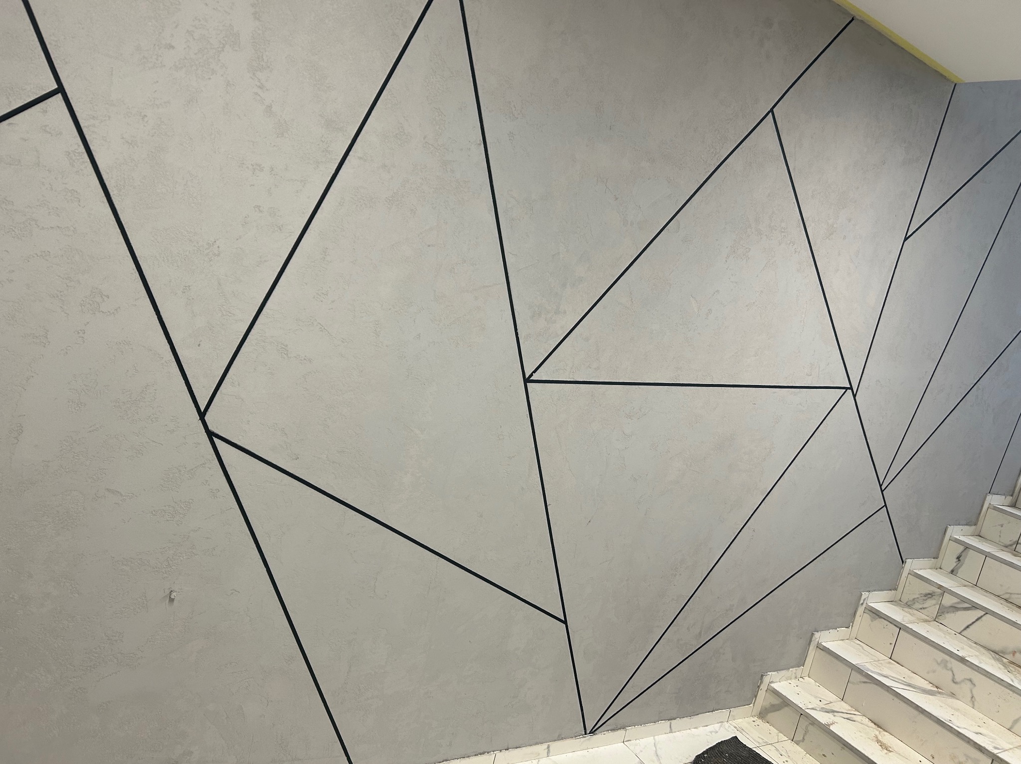 Ściana z dekoracyjną fakturą i geometrycznym wzorem z czarnych linii, widoczne schody z białego marmuru. Nowoczesny design wnętrza.