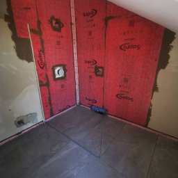PERFECT GLAZ Krzysztof NAGOŃSKI - Łazienka w trakcie remontu: ułożone szare płytki podłogowe, ściany zabezpieczone czerwoną folią w płynie Sopro AEB 640, przygotowane podłoże pod glazurę.