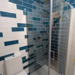 Nowoczesna łazienka po remoncie: biało-granatowe płytki ułożone w pasy, kabina prysznicowa ze szklanymi drzwiami i biała toaleta. Widok na całe wnętrze.