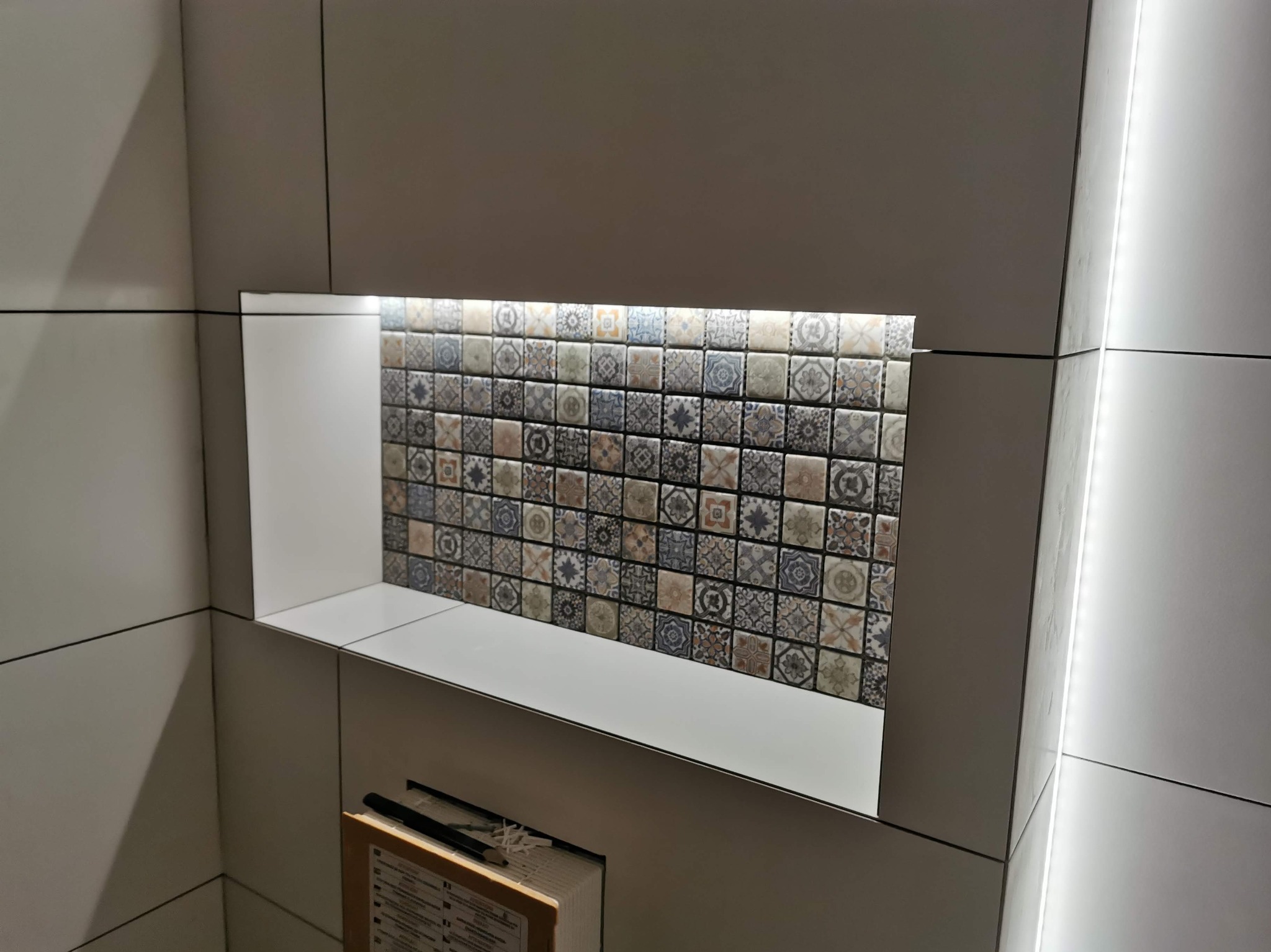 Biała łazienka z wnęką wyłożoną mozaiką w stylu vintage, podświetloną listwą LED. Widoczne fugi i narożniki wykończone z dbałością o detale.