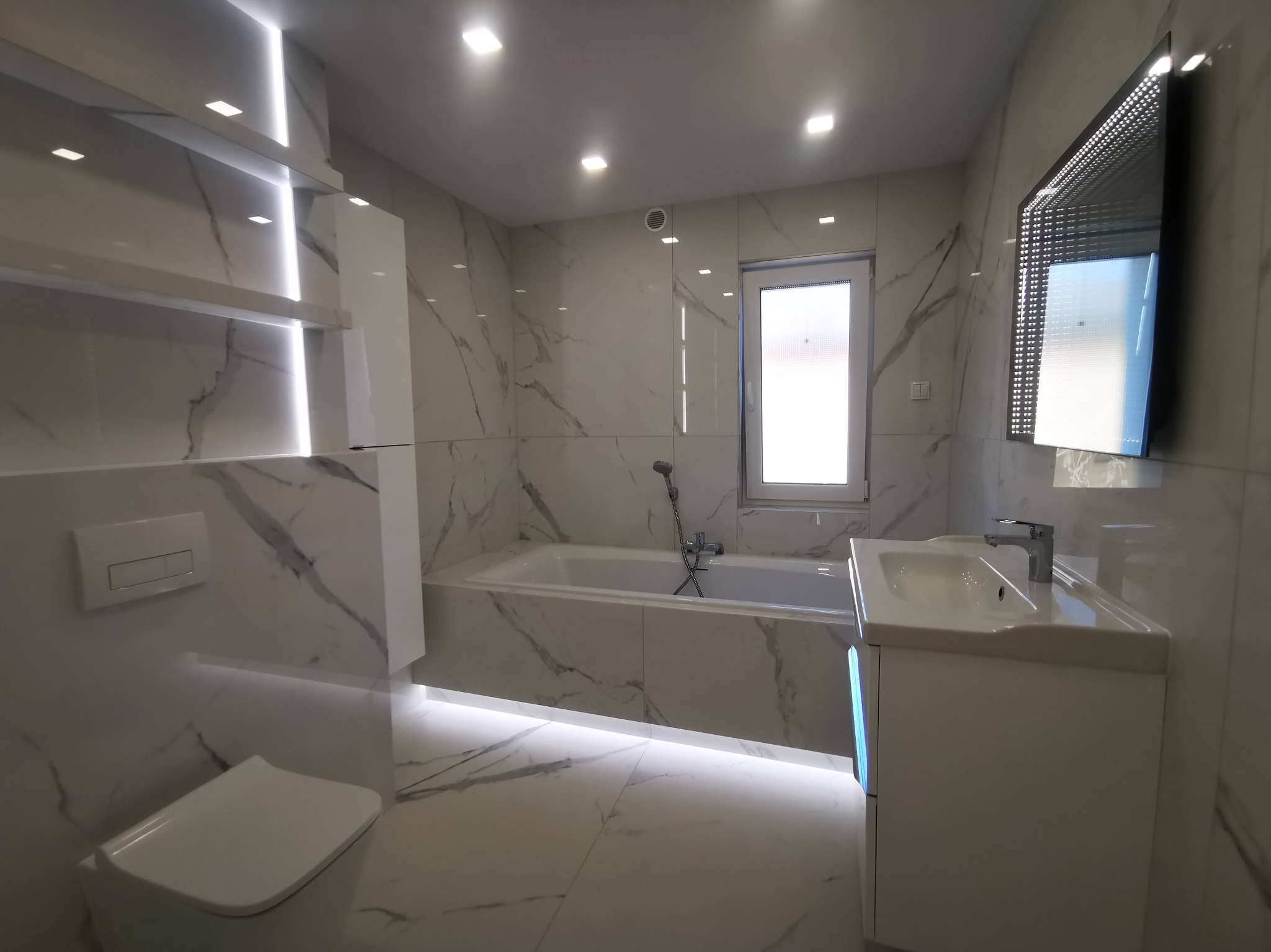 Elegancka łazienka z białymi płytkami imitującymi marmur, podświetleniem LED i lustrem z efektem nieskończoności. Nowoczesny design i minimalistyczny styl.