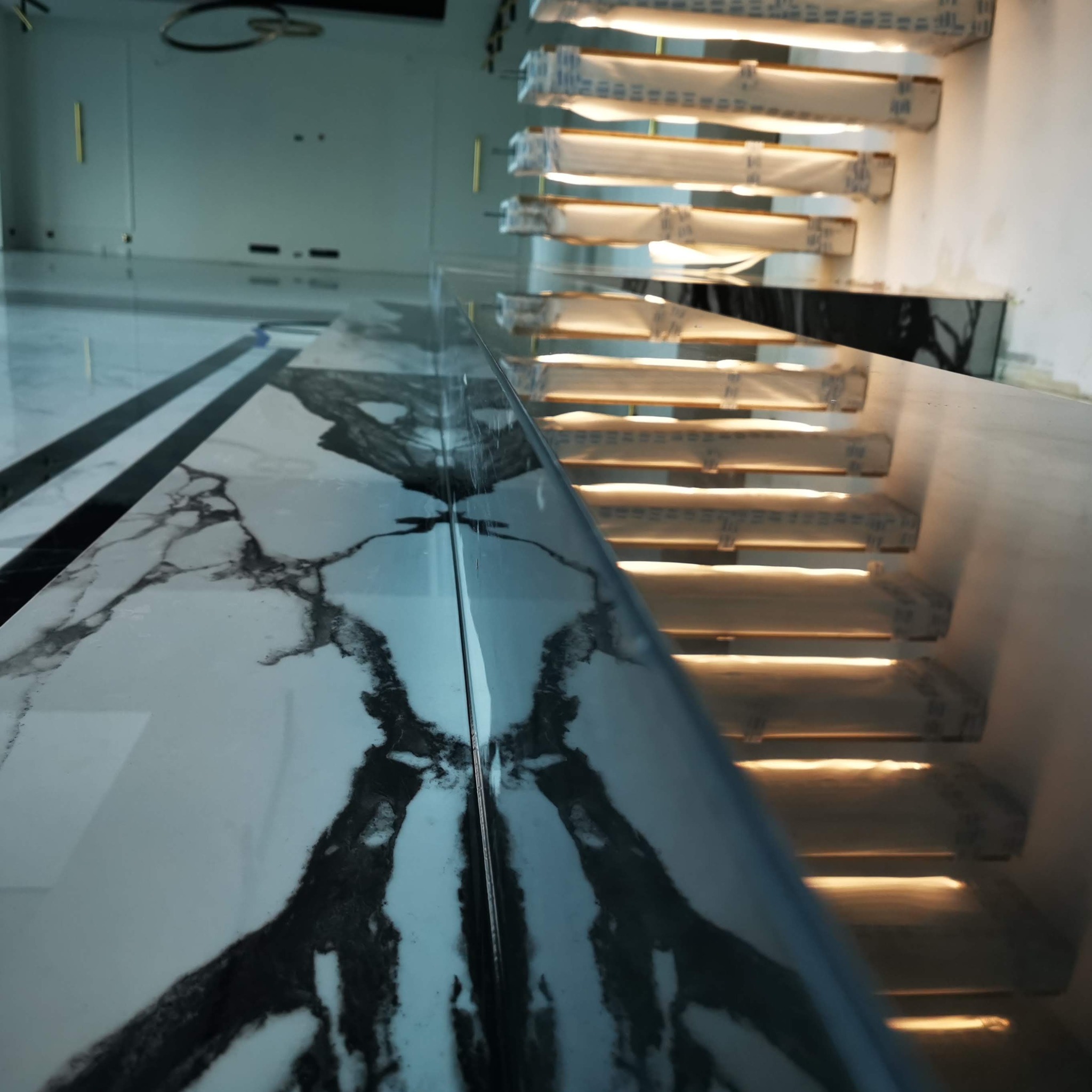 Wykończone schody z marmurowymi stopniami, zabezpieczone folią ochronną, z podświetleniem LED. Widok z góry na wykończoną posadzkę z marmuru.