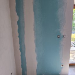 BestBud - Ściana po szpachlowaniu, częściowo pomalowana na niebiesko, widoczne puszki elektryczne. Prace wykończeniowe w Wieluniu.