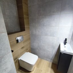 BestBud - Nowoczesna łazienka z podwieszaną toaletą i umywalką, wykończona szarymi i drewnopodobnymi płytkami. Minimalistyczny design, armatura w kolorze czarnym.