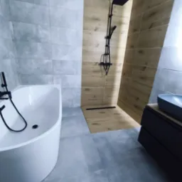 Nowoczesna łazienka z wanną, kabiną prysznicową typu walk-in i szarą płytką podłogową. Czarna armatura i drewnopodobne panele ścienne dodają elegancji.