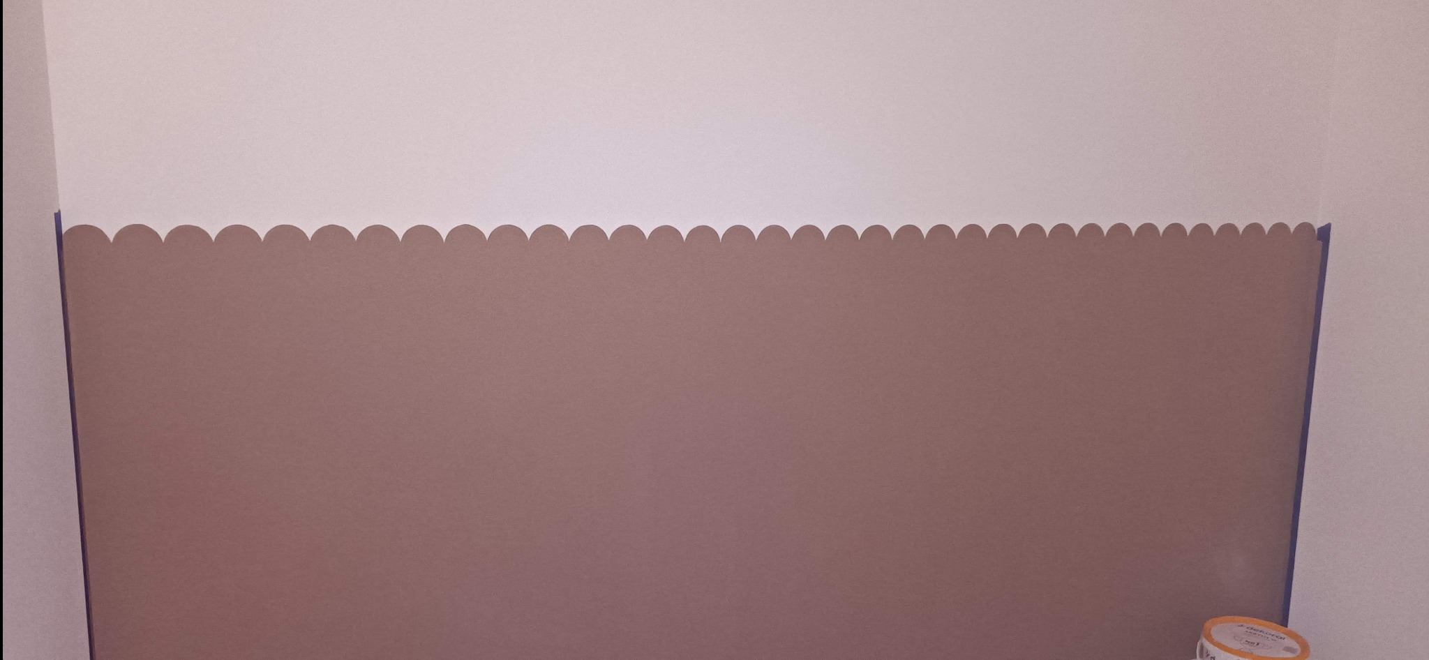 Ściana pomalowana na dwa kolory, z dekoracyjnym wzorem na granicy, zabezpieczona taśmą malarską. Widoczny fragment puszki z farbą.