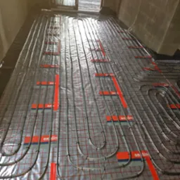 Ułożone rury ogrzewania podłogowego na folii z czerwonymi znacznikami, widok z góry. Równoległe ułożenie rur, przygotowane do zalania posadzką.