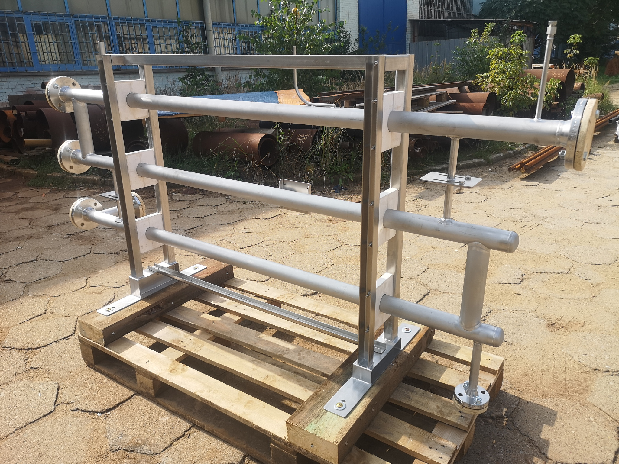 Konstrukcja rurowa ze stali nierdzewnej na palecie, spawana, z widocznymi kołnierzami. Szlifowana powierzchnia, tło przemysłowe.