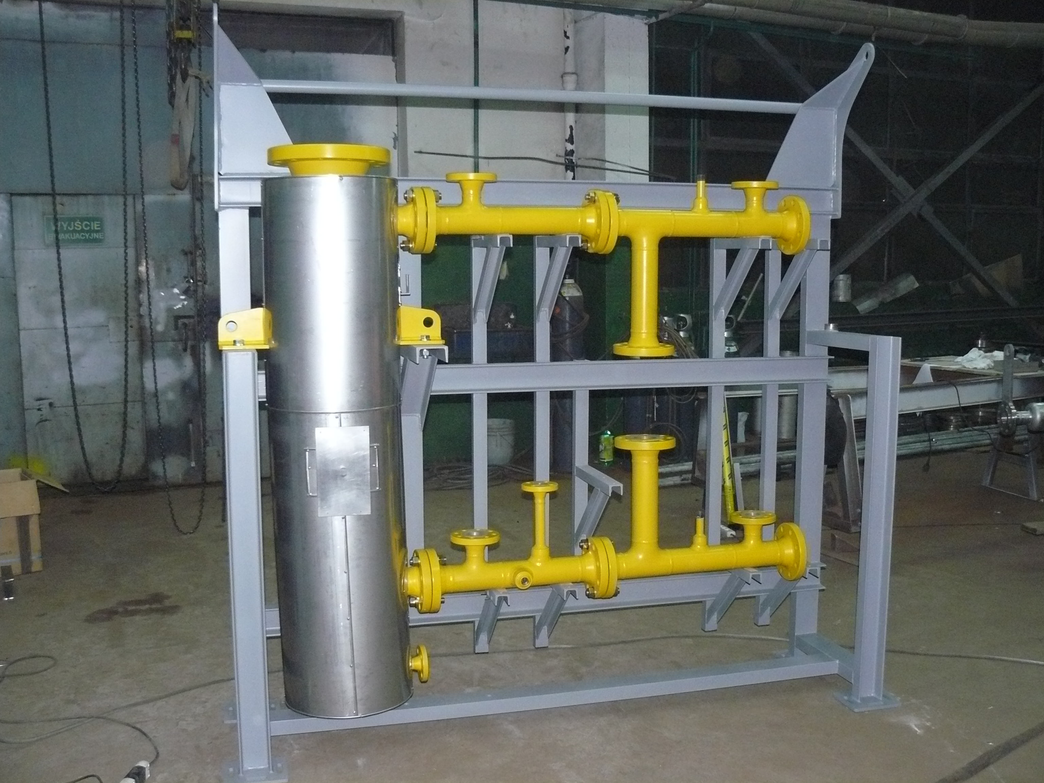 Zespawana konstrukcja stalowa z rurami w kolorze żółtym i zbiornikiem ze stali nierdzewnej. Konstrukcja na szarym tle, widoczne spawy.