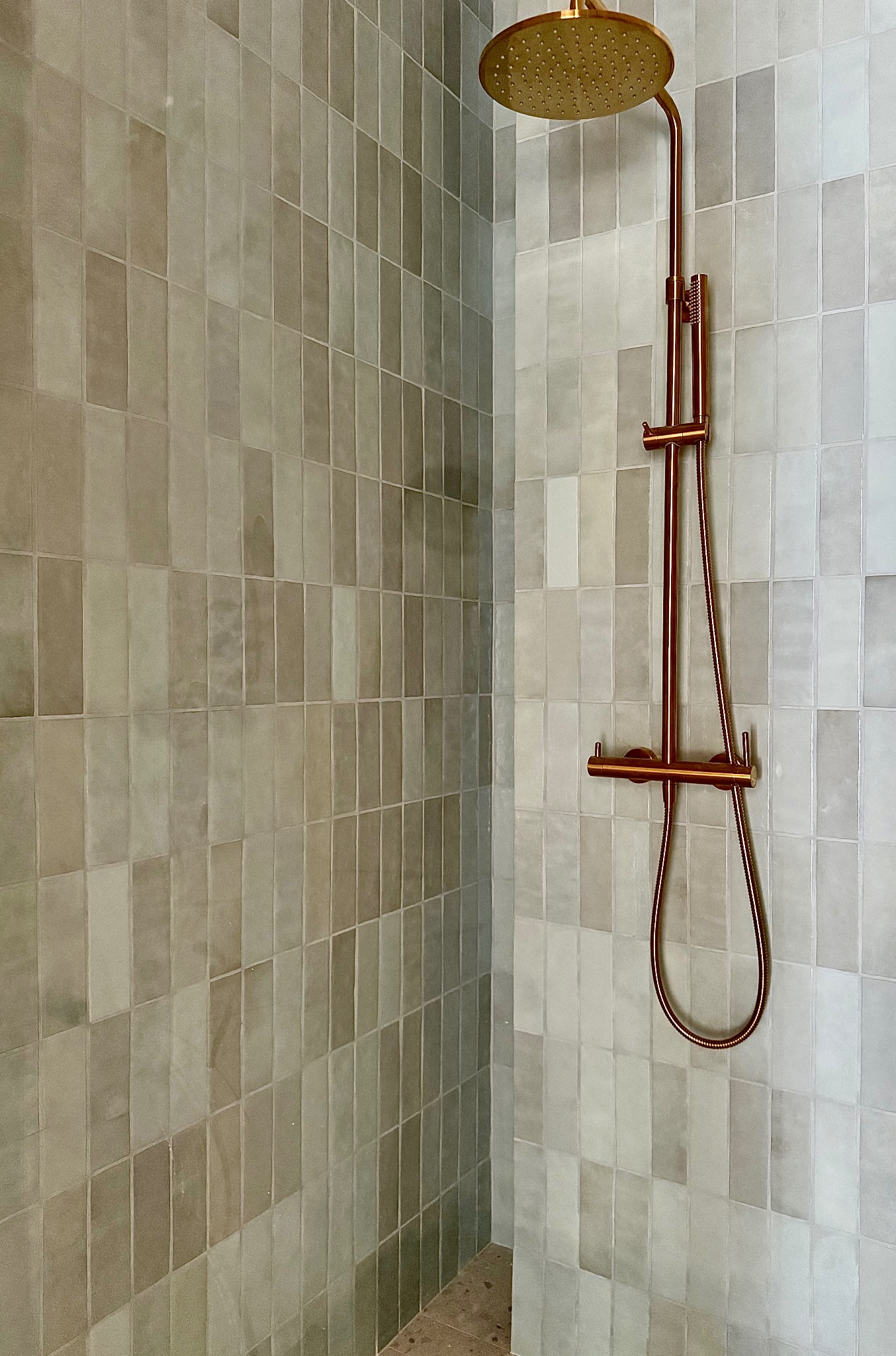 Nowoczesna kabina prysznicowa z miedzianą armaturą i płytkami w odcieniach szarości. Minimalistyczny design, eleganckie wykończenie.