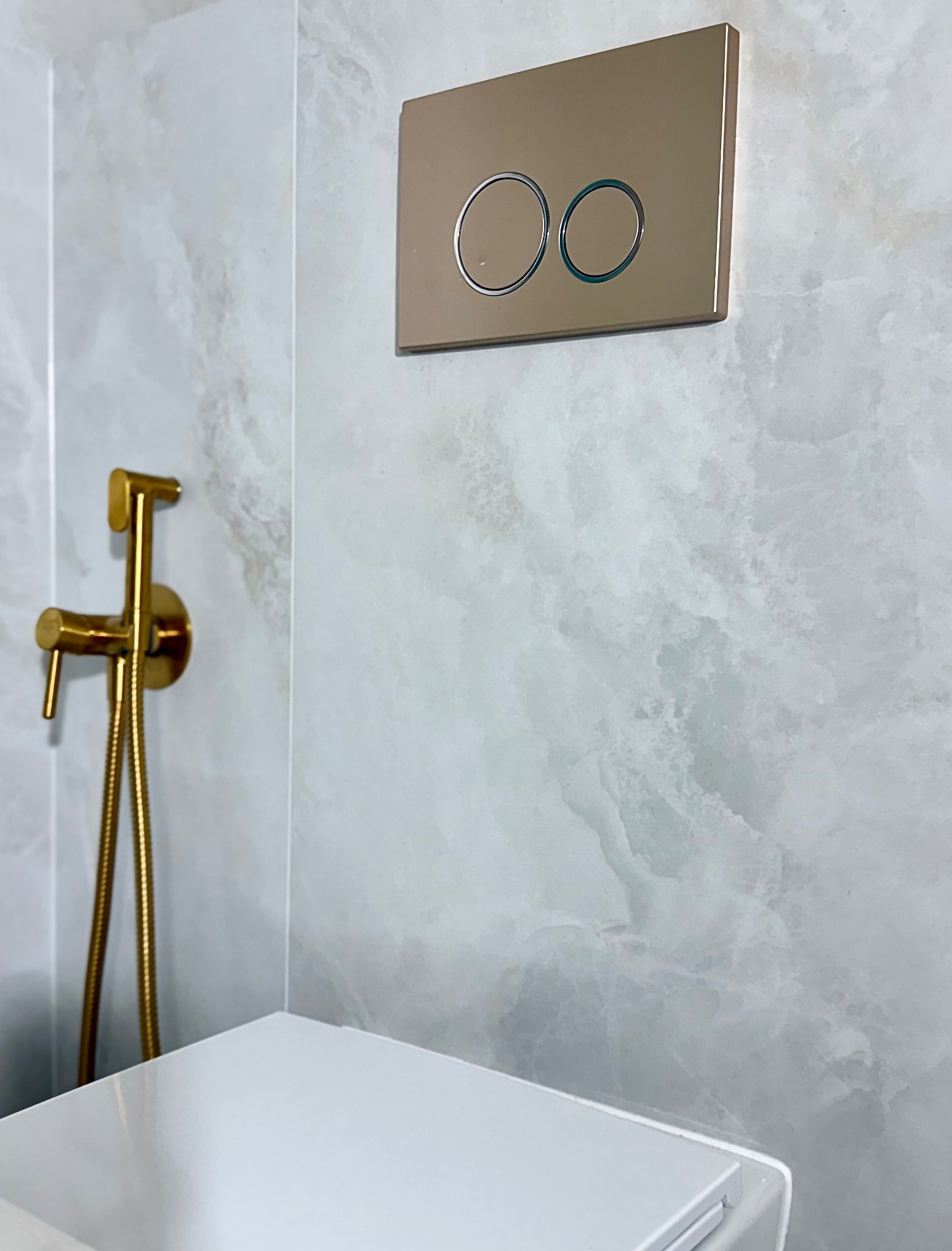 Wykończona łazienka z marmurowymi płytkami, złotą armaturą i przyciskiem spłuczki w kolorze złota. Nowoczesny design.