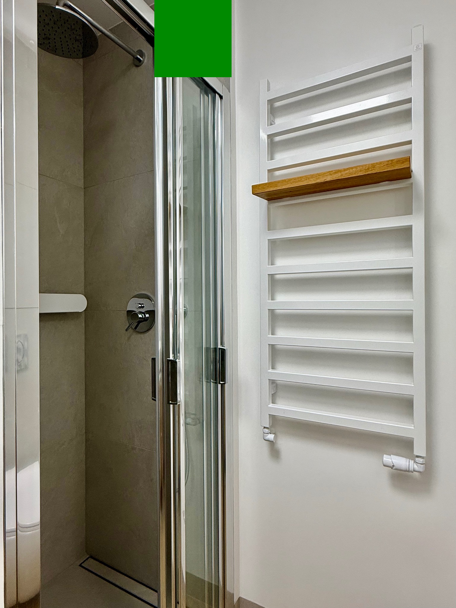 Nowoczesna łazienka z kabiną prysznicową typu walk-in, grzejnikiem drabinkowym z drewnianą półką i szarą płytką imitującą kamień na ścianach.