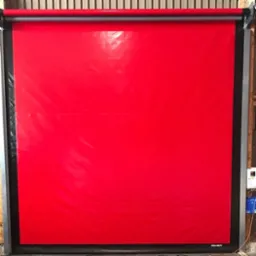 Czerwona, szybkorolowana brama przemysłowa ASSA ABLOY w Rumi. Brama z tworzywa sztucznego, z czarną ramą i sterowaniem elektrycznym po prawej stronie.