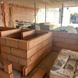 Budowa domu w Zakopanem: wznoszenie ścian z czerwonej cegły ceramicznej. Widoczne worki z zaprawą murarską i drewniane deski.