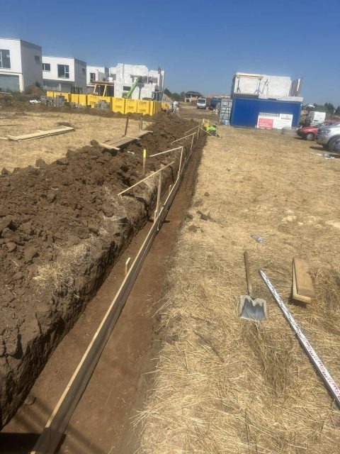 Wykonany wykop pod fundament z deskowaniem i narzędziami w tle budowa domów jednorodzinnych i budynek w trakcie budowy.