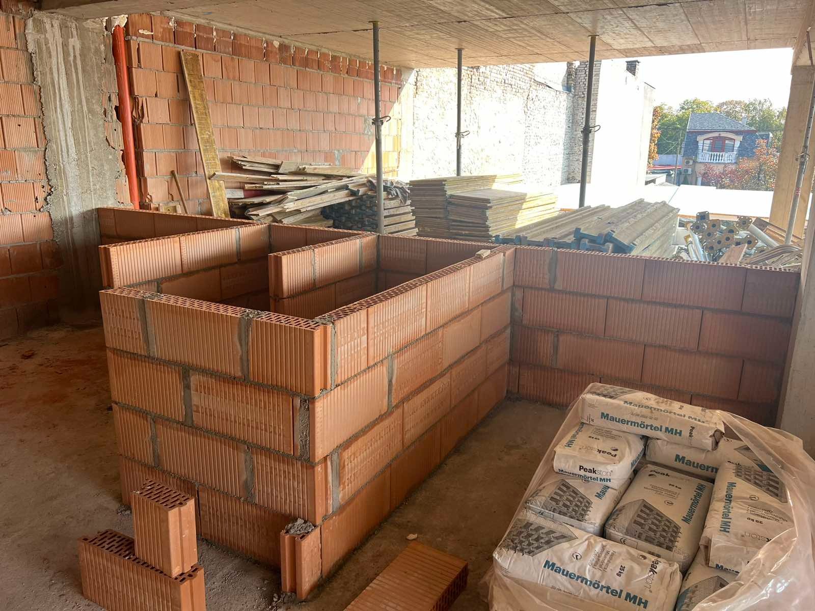 Budowa domu w Zakopanem: wznoszenie ścian z czerwonej cegły ceramicznej. Widoczne worki z zaprawą murarską i drewniane deski.