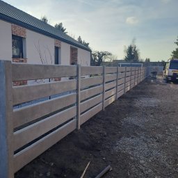 Markowe Ogrodzenia Betonowe Marek Januszewski - Nowoczesne ogrodzenie betonowe z poziomymi przęsłami, świeżo po montażu. Widoczny budynek w tle i częściowo samochód dostawczy.