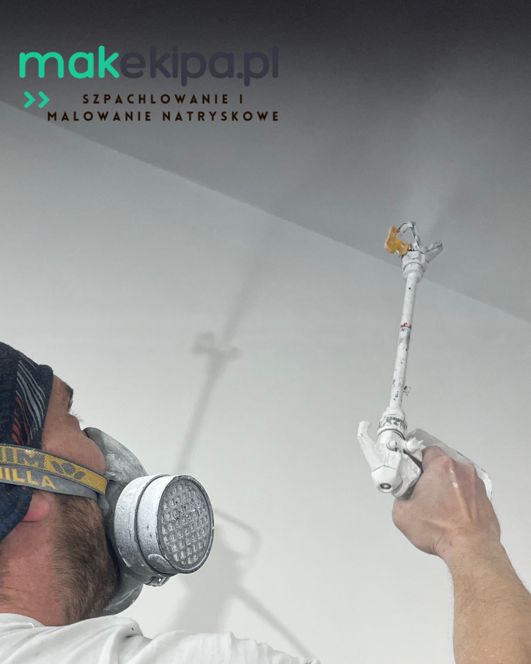 Malowanie natryskowe sufitu przez pracownika w masce ochronnej. Widoczny pistolet natryskowy i świeżo pomalowana, gładka powierzchnia. Praca w toku.