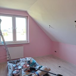 Mateos - Pokój na poddaszu po malowaniu ścian na delikatny róż, z widocznymi narzędziami i farbami, drabina oparta o okno, jasna podłoga.