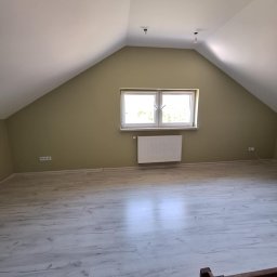 Mateos - Poddasze po remoncie: świeżo pomalowane ściany w odcieniach zieleni, jasne panele podłogowe imitujące drewno, biały grzejnik pod oknem. Widoczne gniazdka elektryczne.