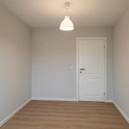 Mateos - Jasne wnętrze pokoju po remoncie: drewnopodobne panele podłogowe, białe drzwi z srebrną klamką, szare ściany i nowoczesna lampa sufitowa. Minimalistyczny design.